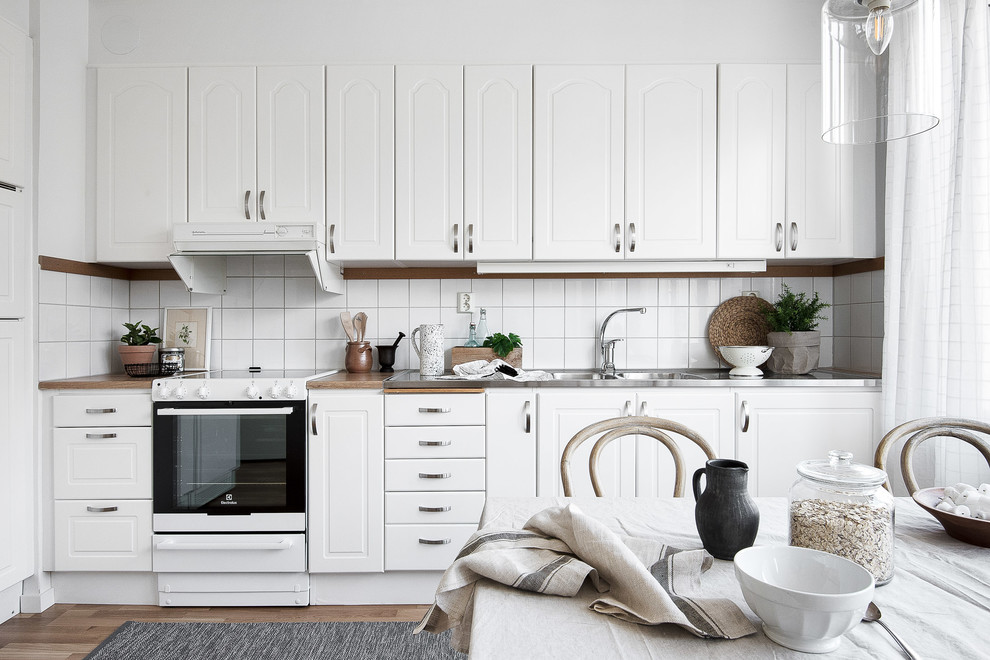 Einzeilige Skandinavische Wohnküche ohne Insel mit Doppelwaschbecken, profilierten Schrankfronten, weißen Schränken, Küchenrückwand in Weiß, braunem Holzboden, braunem Boden und brauner Arbeitsplatte in Stockholm