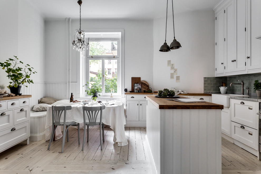 This is an example of a medium sized classic l-shaped kitchen/diner in Stockholm with a belfast sink, shaker cabinets, white cabinets, grey splashback, light hardwood flooring and an island.