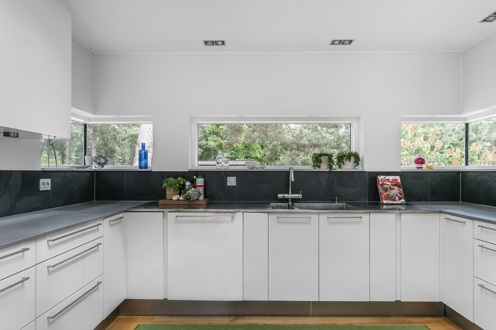 Modern inredning av ett mellanstort grå grått u-kök, med en integrerad diskho, släta luckor, mellanmörkt trägolv och brunt golv