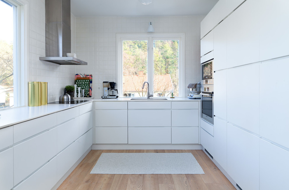 Foto på ett avskilt, mellanstort funkis l-kök, med släta luckor, vita skåp, vitt stänkskydd, rostfria vitvaror, ljust trägolv, en enkel diskho och laminatbänkskiva