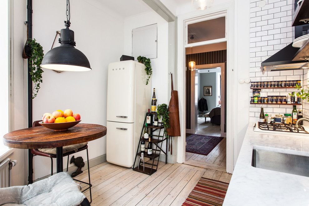 Einzeilige, Mittelgroße Skandinavische Wohnküche ohne Insel mit Unterbauwaschbecken, Küchenrückwand in Weiß, Rückwand aus Metrofliesen und hellem Holzboden in Stockholm