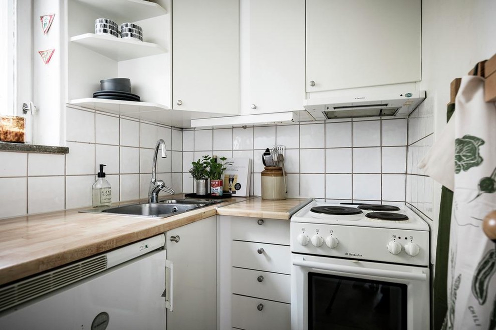 Design ideas for a small scandi l-shaped kitchen in Stockholm with a built-in sink, flat-panel cabinets, white cabinets, wood worktops, white splashback, white appliances and brown worktops.