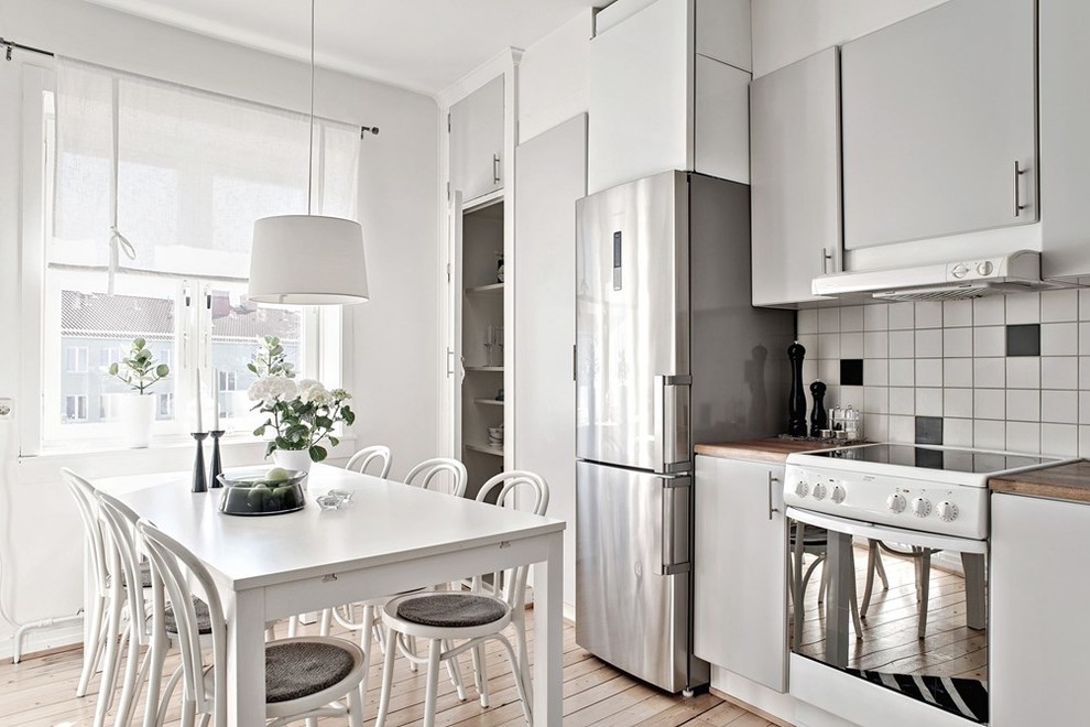 Nordisk inredning av ett stort linjärt kök och matrum, med släta luckor, grå skåp, flerfärgad stänkskydd, vita vitvaror, ljust trägolv och träbänkskiva