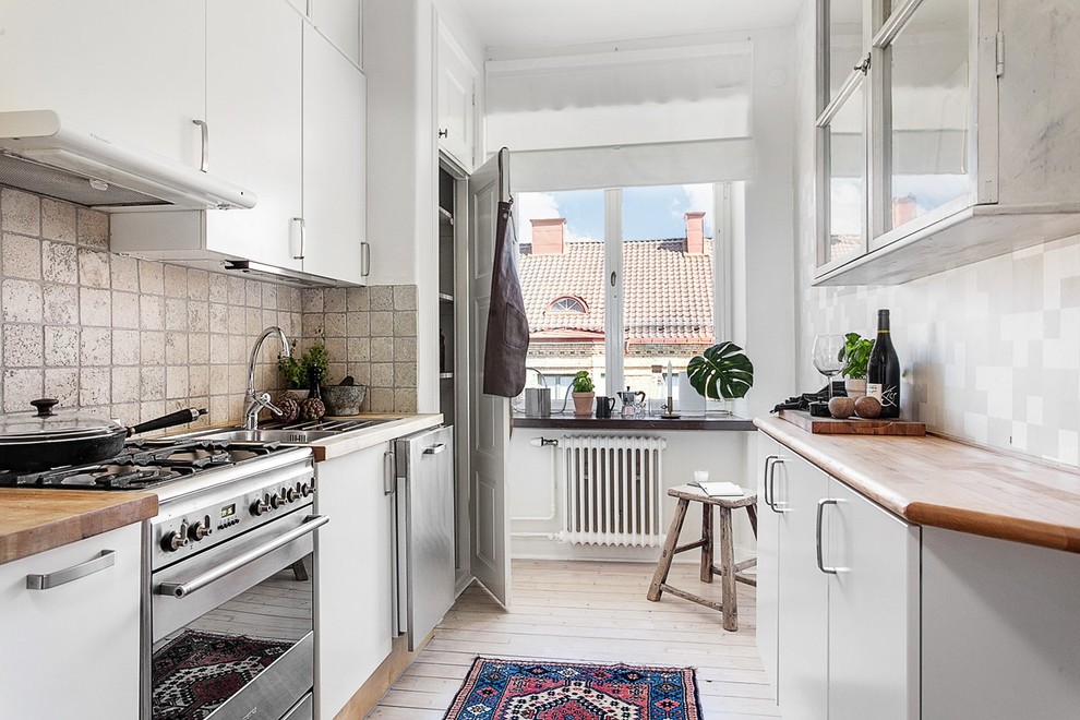 This is an example of a medium sized scandi galley enclosed kitchen in Gothenburg with a single-bowl sink, flat-panel cabinets, white cabinets, wood worktops, stainless steel appliances, light hardwood flooring and no island.