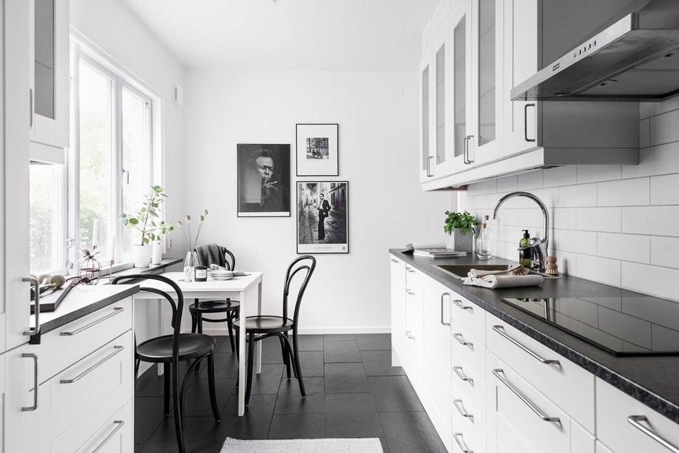 Foto på ett stort minimalistiskt kök, med en nedsänkt diskho, vitt stänkskydd, stänkskydd i tunnelbanekakel, luckor med glaspanel, granitbänkskiva och klinkergolv i keramik