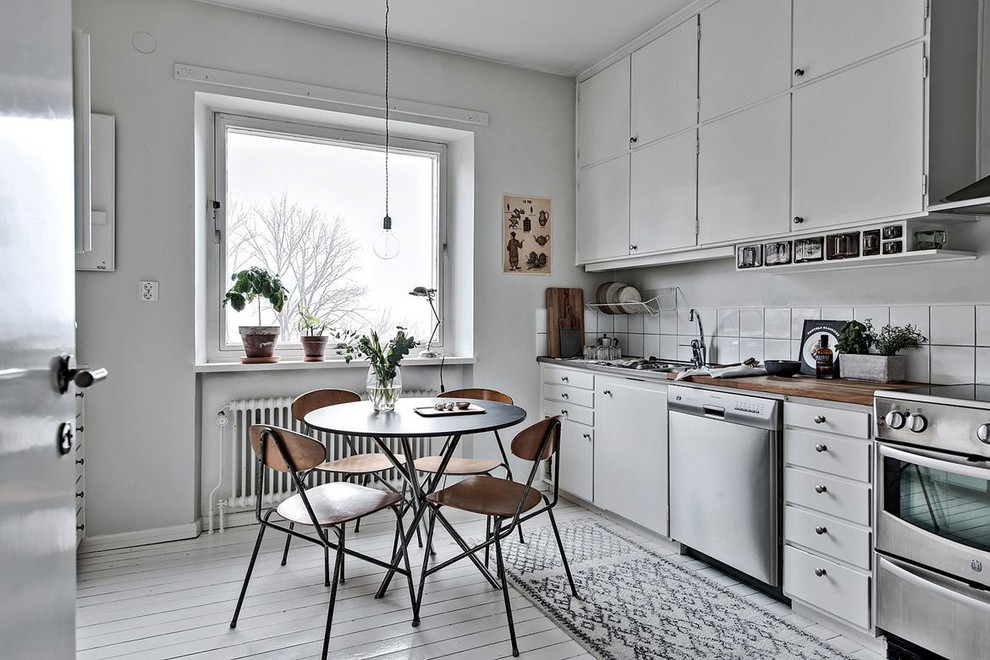 Einzeilige, Mittelgroße Skandinavische Küche ohne Insel mit flächenbündigen Schrankfronten, weißen Schränken, Arbeitsplatte aus Holz, Küchenrückwand in Weiß und gebeiztem Holzboden in Göteborg