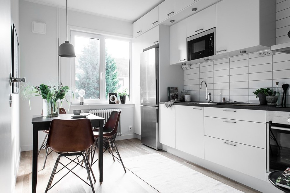 Mid-sized danish single-wall light wood floor eat-in kitchen photo in Gothenburg with a drop-in sink, flat-panel cabinets, white cabinets, white backsplash, subway tile backsplash and stainless steel appliances