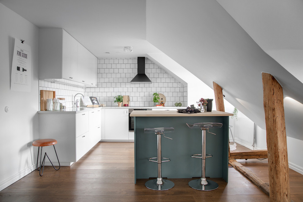 Minimalistisk inredning av ett litet kök, med släta luckor, vita skåp, vitt stänkskydd, en köksö, rostfria vitvaror, mellanmörkt trägolv och brunt golv