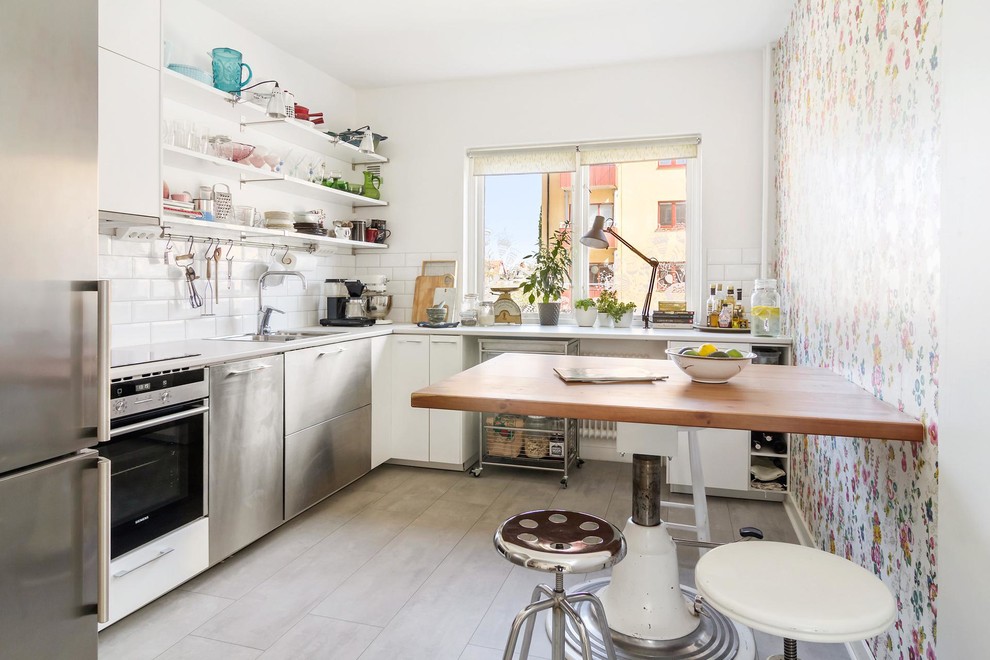 Inspiration for a medium sized scandi l-shaped enclosed kitchen in Orebro with a double-bowl sink, flat-panel cabinets, white cabinets, white splashback, metro tiled splashback, stainless steel appliances, laminate countertops, limestone flooring and no island.