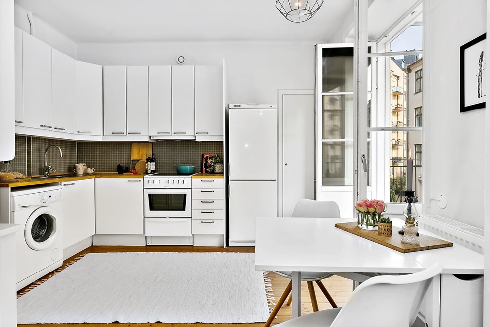 Medium sized traditional l-shaped open plan kitchen in Stockholm with flat-panel cabinets, white cabinets, wood worktops, white appliances, medium hardwood flooring and no island.