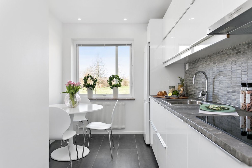 Immagine di una cucina scandinava con lavello a doppia vasca, ante lisce, ante bianche, top in granito, paraspruzzi grigio, elettrodomestici bianchi, pavimento in ardesia e nessuna isola