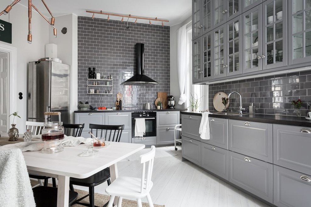 Inredning av ett skandinaviskt mellanstort kök, med luckor med glaspanel, grå skåp, grått stänkskydd, stänkskydd i tunnelbanekakel, svarta vitvaror och målat trägolv