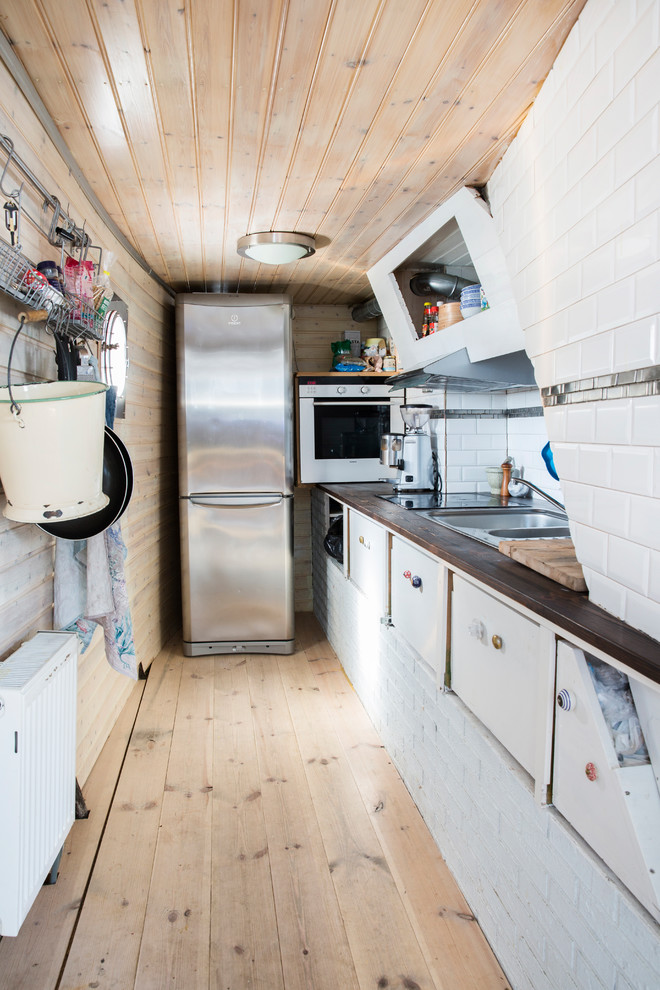 Foto på ett avskilt industriellt linjärt kök, med släta luckor, träbänkskiva, vitt stänkskydd, rostfria vitvaror, ljust trägolv och beiget golv