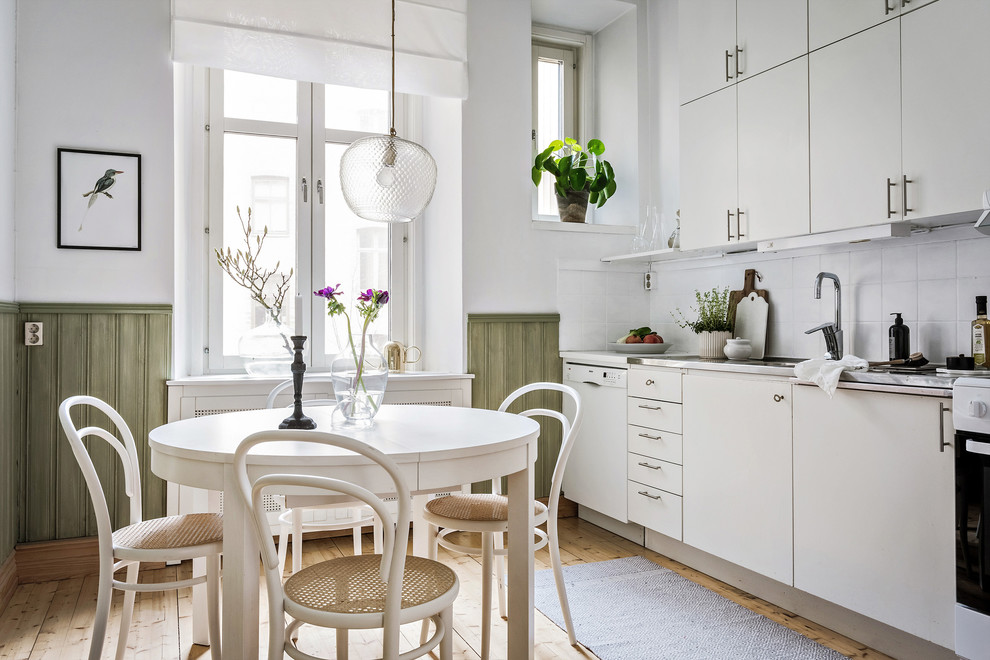 Bild på ett mellanstort minimalistiskt linjärt kök och matrum, med släta luckor, vita skåp, bänkskiva i rostfritt stål, vitt stänkskydd, beiget golv och ljust trägolv