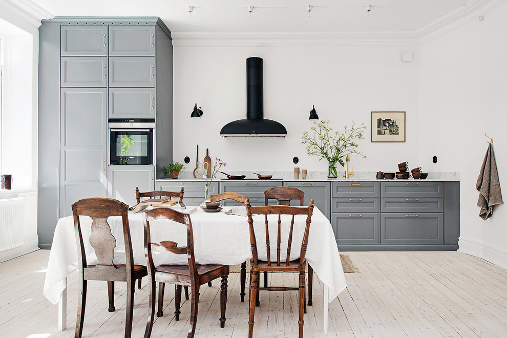 Пример оригинального дизайна: большая прямая кухня в скандинавском стиле с обеденным столом, фасадами с утопленной филенкой, серыми фасадами, черной техникой, светлым паркетным полом и мраморной столешницей без острова