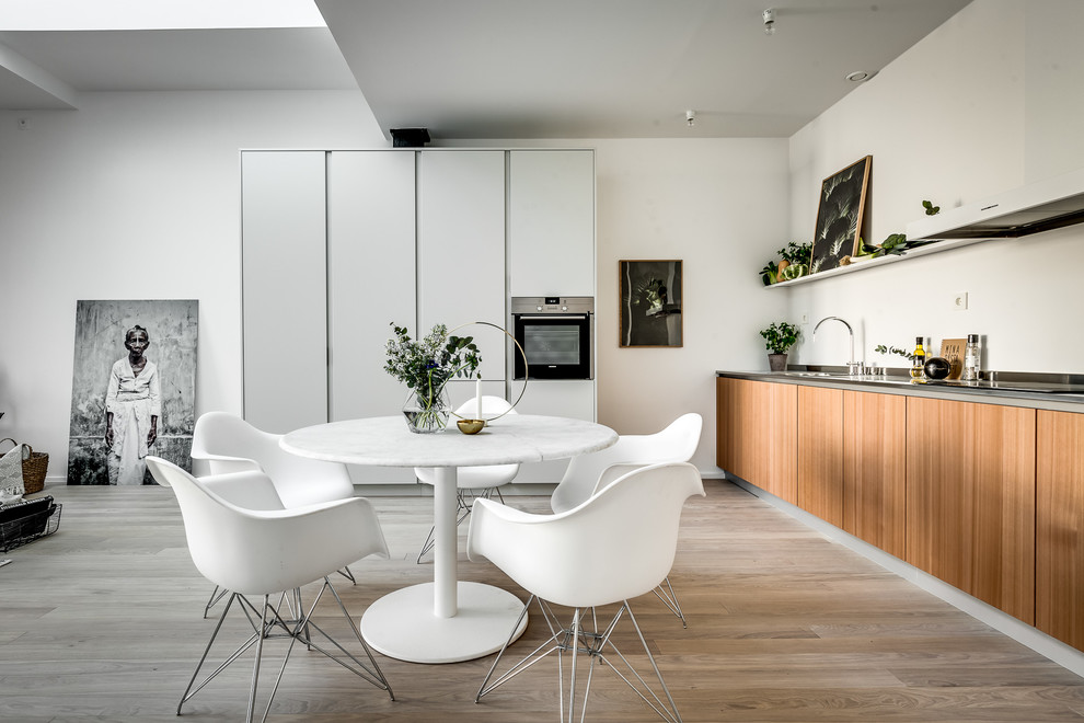 Large scandinavian l-shaped open plan kitchen in Stockholm with flat-panel cabinets, stainless steel appliances, light hardwood flooring, no island, beige floors, medium wood cabinets and white splashback.