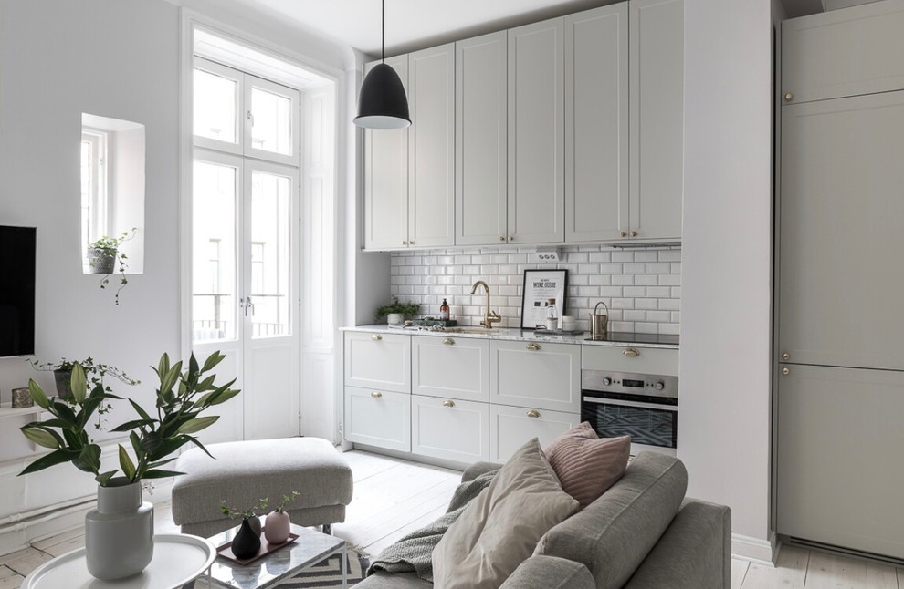 Exempel på ett minimalistiskt grå linjärt grått kök med öppen planlösning, med en undermonterad diskho, skåp i shakerstil, grå skåp, vitt stänkskydd, stänkskydd i tunnelbanekakel, integrerade vitvaror, ljust trägolv och beiget golv