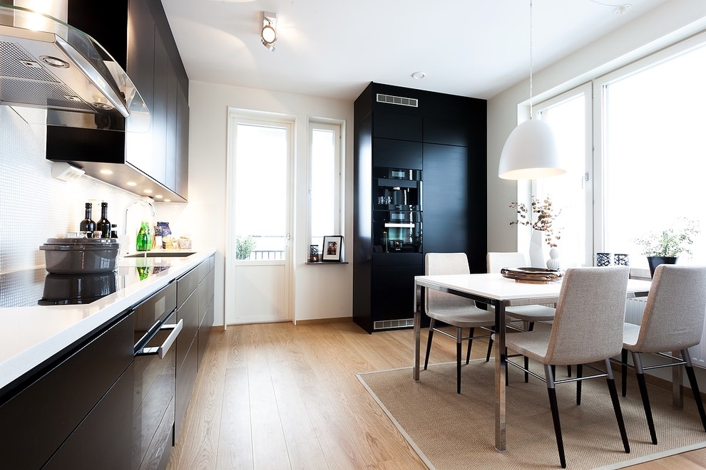 Design ideas for a medium sized contemporary single-wall kitchen/diner in Gothenburg with a single-bowl sink, flat-panel cabinets, black cabinets, white splashback, mosaic tiled splashback, black appliances, light hardwood flooring, no island and brown floors.