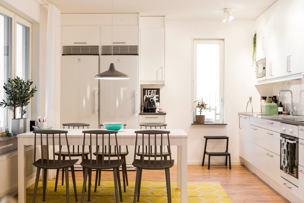 Medium sized scandi kitchen/diner in Gothenburg with an integrated sink, flat-panel cabinets, white cabinets, stainless steel worktops, white appliances, light hardwood flooring and no island.