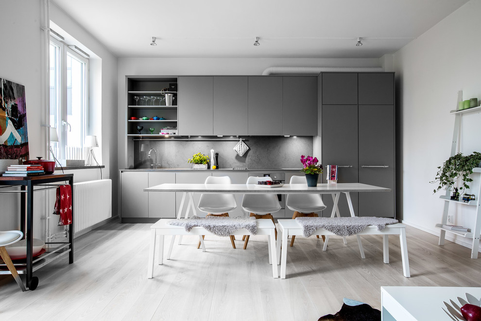 Идея дизайна: прямая кухня среднего размера в скандинавском стиле с обеденным столом, плоскими фасадами, серыми фасадами, серым фартуком и светлым паркетным полом без острова