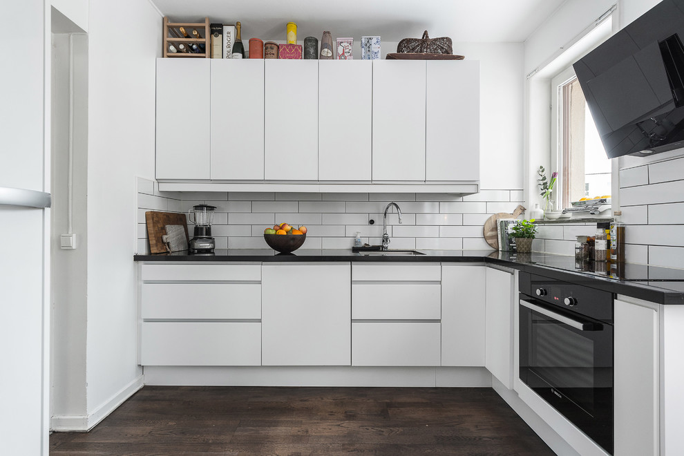 Idéer för mellanstora, avskilda skandinaviska svart l-kök, med släta luckor, vita skåp, vitt stänkskydd, mörkt trägolv, brunt golv, en undermonterad diskho och svarta vitvaror