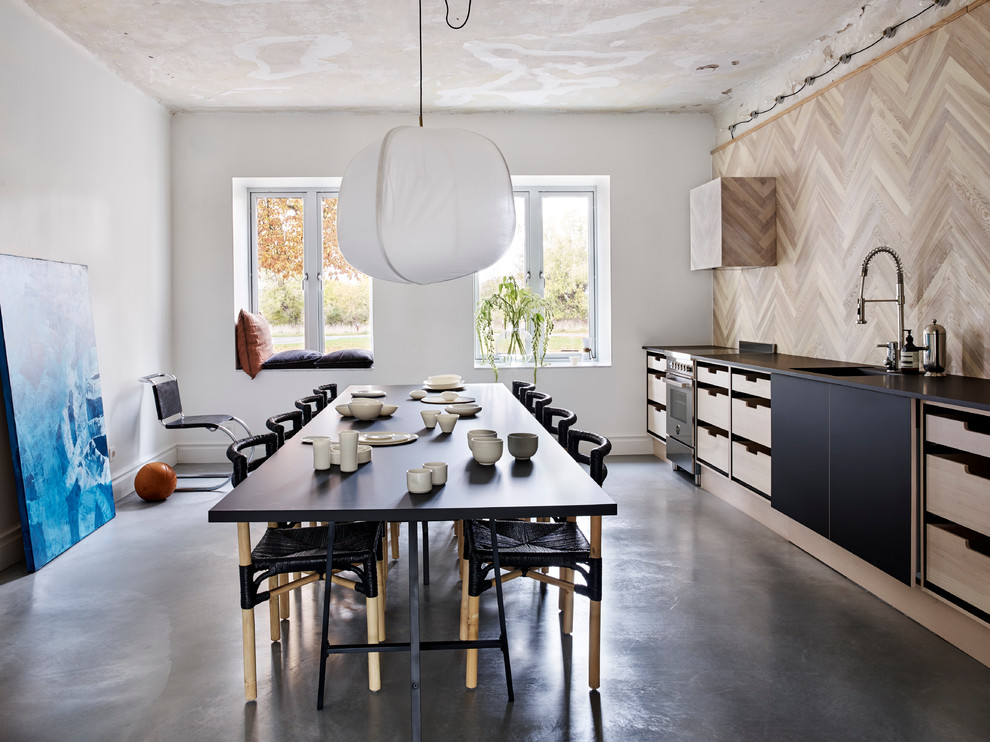 マルメにある高級な広いコンテンポラリースタイルのおしゃれなキッチン (黒いキャビネット、木材のキッチンパネル、コンクリートの床、アイランドなし、シングルシンク) の写真