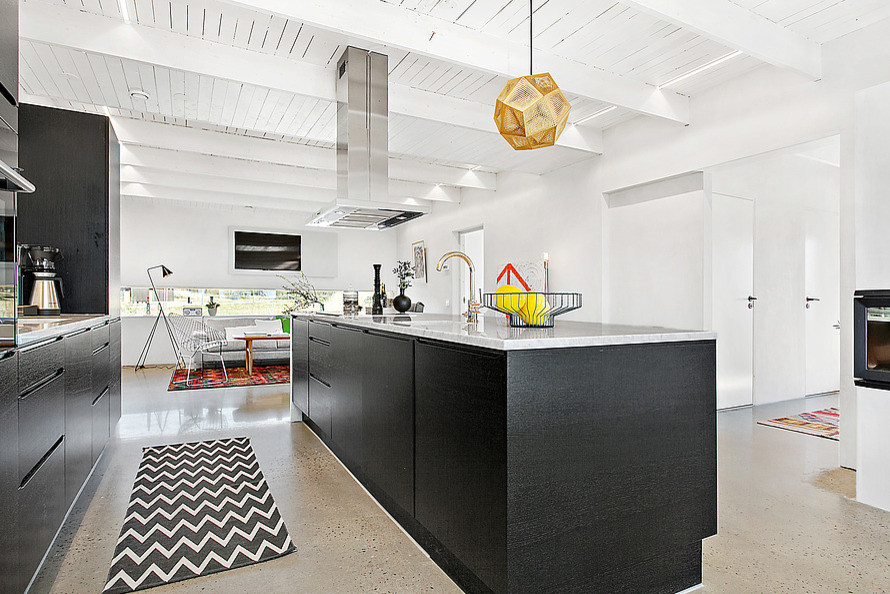 Modern inredning av ett stort kök, med släta luckor, svarta skåp, marmorbänkskiva, grått stänkskydd, svarta vitvaror, betonggolv och en köksö