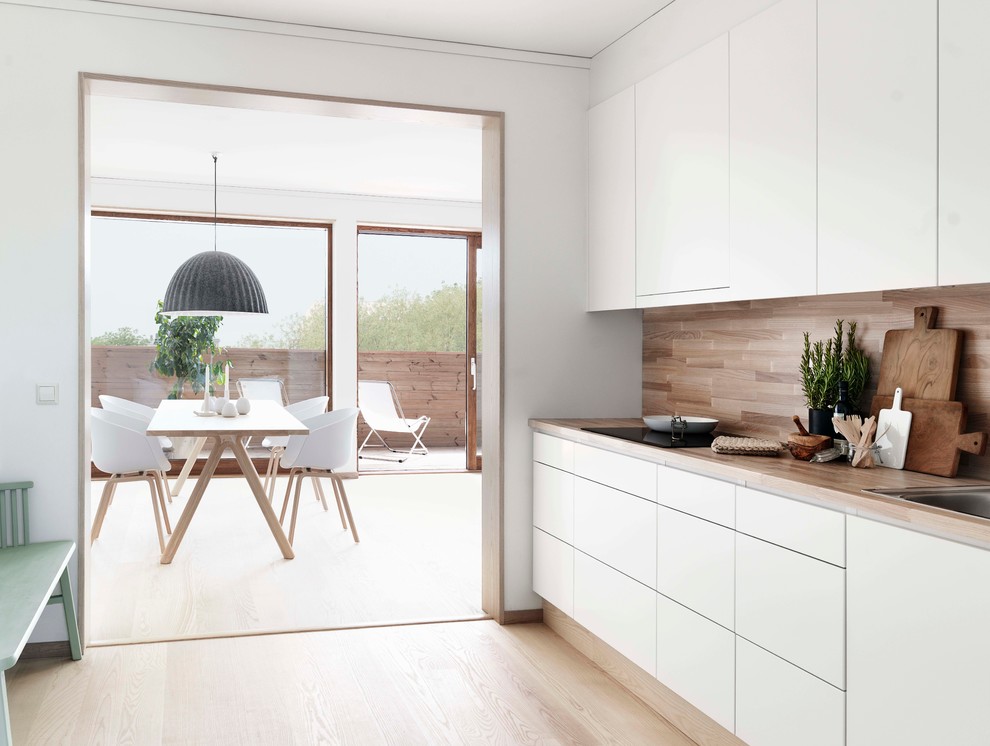 Foto de cocina comedor lineal nórdica de tamaño medio sin isla con armarios con paneles lisos, puertas de armario blancas, encimera de madera, electrodomésticos blancos, suelo de madera clara y fregadero encastrado