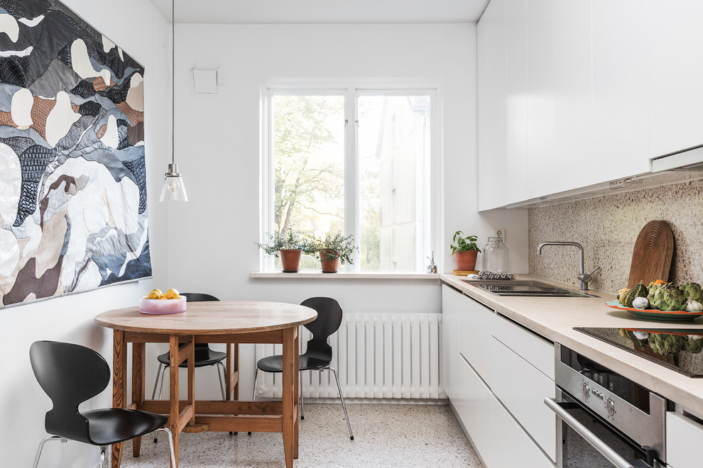 Einzeilige, Mittelgroße Nordische Wohnküche ohne Insel mit Doppelwaschbecken, weißen Schränken, Arbeitsplatte aus Holz, Küchengeräten aus Edelstahl, Terrazzo-Boden und flächenbündigen Schrankfronten in Göteborg