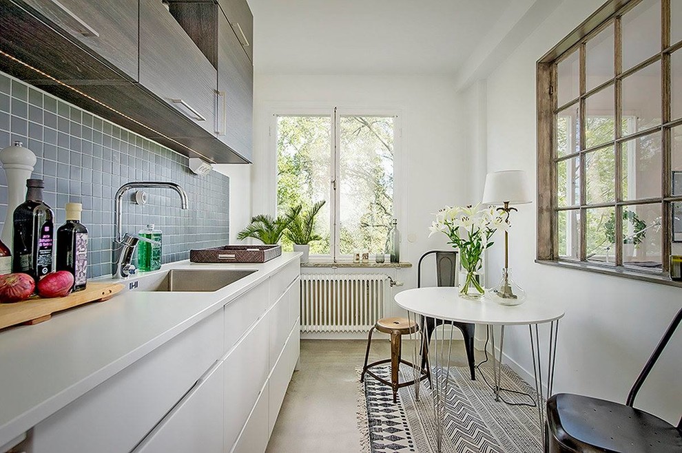 Skandinavisk inredning av ett mellanstort linjärt kök och matrum, med en undermonterad diskho, släta luckor, vita skåp, grått stänkskydd och betonggolv