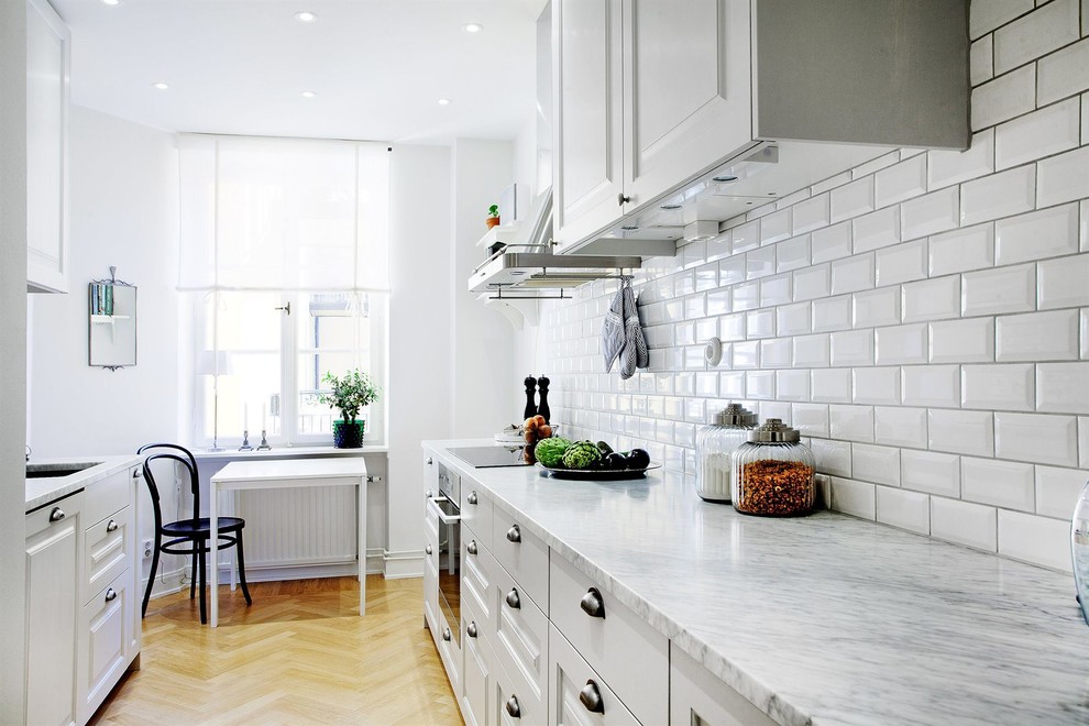 Inspiration for a mid-sized scandinavian galley medium tone wood floor eat-in kitchen remodel in Stockholm with raised-panel cabinets, white cabinets, white backsplash, subway tile backsplash, a drop-in sink, marble countertops, stainless steel appliances and no island