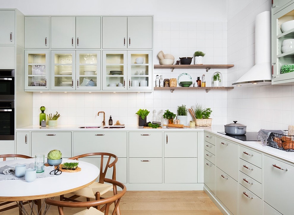 Design ideas for a medium sized scandi l-shaped kitchen/diner in Gothenburg with a double-bowl sink, flat-panel cabinets, green cabinets, white splashback, light hardwood flooring, marble worktops and porcelain splashback.