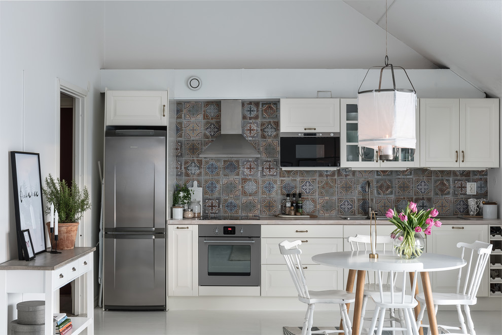 Foto på ett stort nordiskt linjärt kök och matrum, med luckor med upphöjd panel, vita skåp, flerfärgad stänkskydd, rostfria vitvaror och målat trägolv
