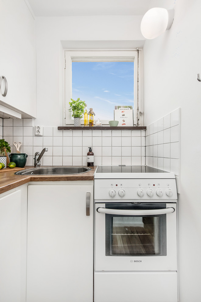 Small scandinavian l-shaped separate kitchen in Stockholm with a single-bowl sink, flat-panel cabinets, white cabinets, wood benchtops, white splashback, white appliances, porcelain splashback and no island.