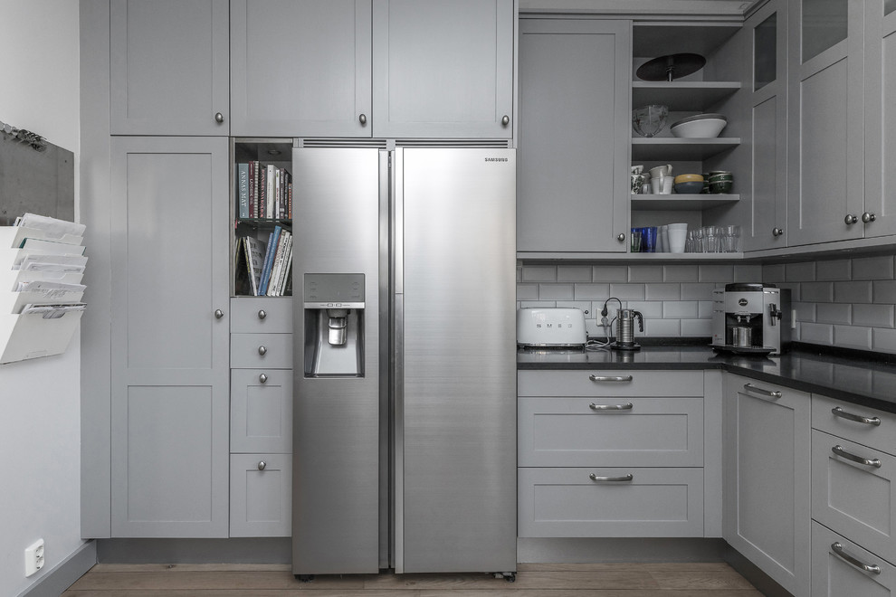 Cette image montre une cuisine nordique de taille moyenne avec un placard avec porte à panneau encastré, des portes de placard grises et une crédence noire.