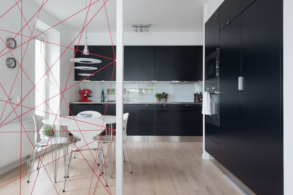Example of a mid-sized danish l-shaped light wood floor and beige floor open concept kitchen design in Gothenburg with a drop-in sink, flat-panel cabinets, black cabinets, blue backsplash, mosaic tile backsplash, black appliances and no island