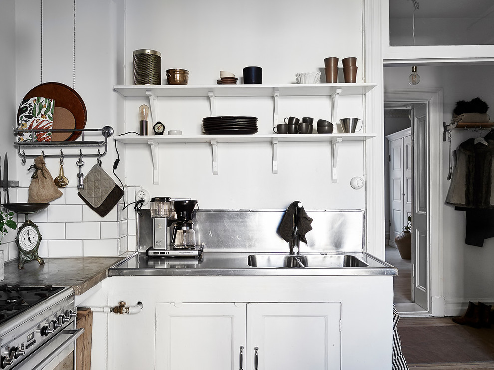 Bild på ett avskilt, litet skandinaviskt l-kök, med luckor med infälld panel, vita skåp och bänkskiva i rostfritt stål
