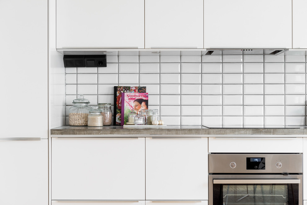 Inspiration for a large modern single-wall kitchen/diner in Gothenburg with a single-bowl sink, flat-panel cabinets, white cabinets, concrete worktops, white splashback, ceramic splashback, white appliances, light hardwood flooring and no island.