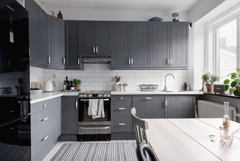 Exempel på ett mellanstort nordiskt kök, med en nedsänkt diskho, luckor med profilerade fronter, grå skåp, laminatbänkskiva, vitt stänkskydd, stänkskydd i keramik, svarta vitvaror, ljust trägolv och vitt golv