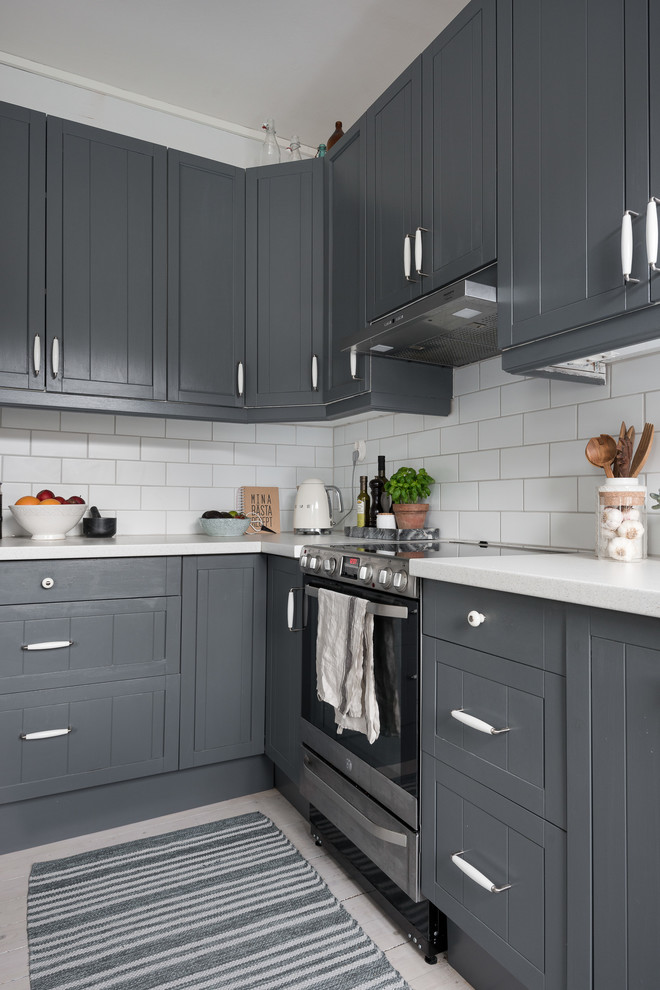 This is an example of a medium sized scandinavian l-shaped open plan kitchen in Gothenburg with a built-in sink, beaded cabinets, grey cabinets, laminate countertops, white splashback, ceramic splashback, black appliances, light hardwood flooring, no island and white floors.