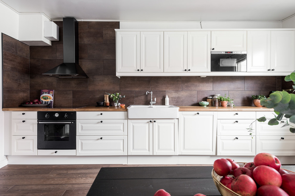 Idéer för ett skandinaviskt kök, med en dubbel diskho, vita skåp, träbänkskiva, brunt stänkskydd, stänkskydd i keramik, vita vitvaror, mörkt trägolv och luckor med upphöjd panel