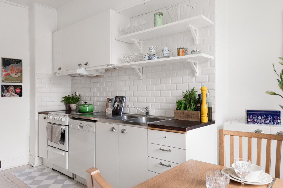 Foto på ett mellanstort nordiskt brun linjärt kök och matrum, med en dubbel diskho, vita skåp, vitt stänkskydd, stänkskydd i porslinskakel, vita vitvaror, målat trägolv, vitt golv och släta luckor