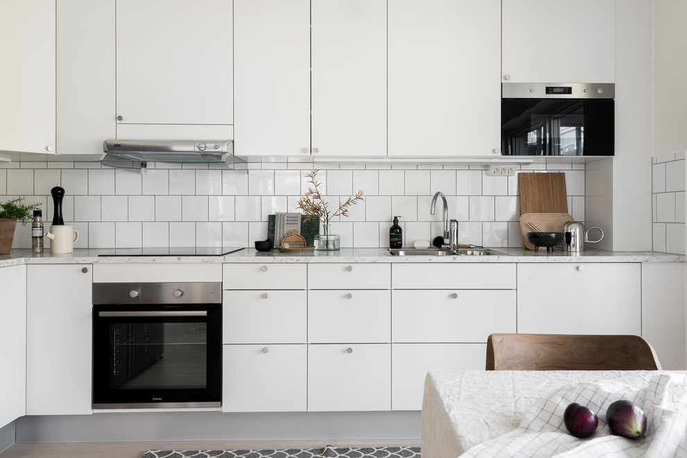 Idéer för att renovera ett mellanstort minimalistiskt grå grått kök, med en nedsänkt diskho, släta luckor, vita skåp, laminatbänkskiva, vitt stänkskydd, stänkskydd i keramik, rostfria vitvaror och ljust trägolv