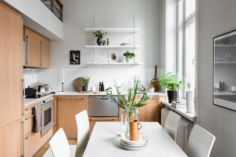 Foto de cocina escandinava de tamaño medio con armarios con paneles lisos, puertas de armario de madera oscura, salpicadero blanco, electrodomésticos de acero inoxidable, suelo de madera en tonos medios, una isla y salpicadero de azulejos de porcelana