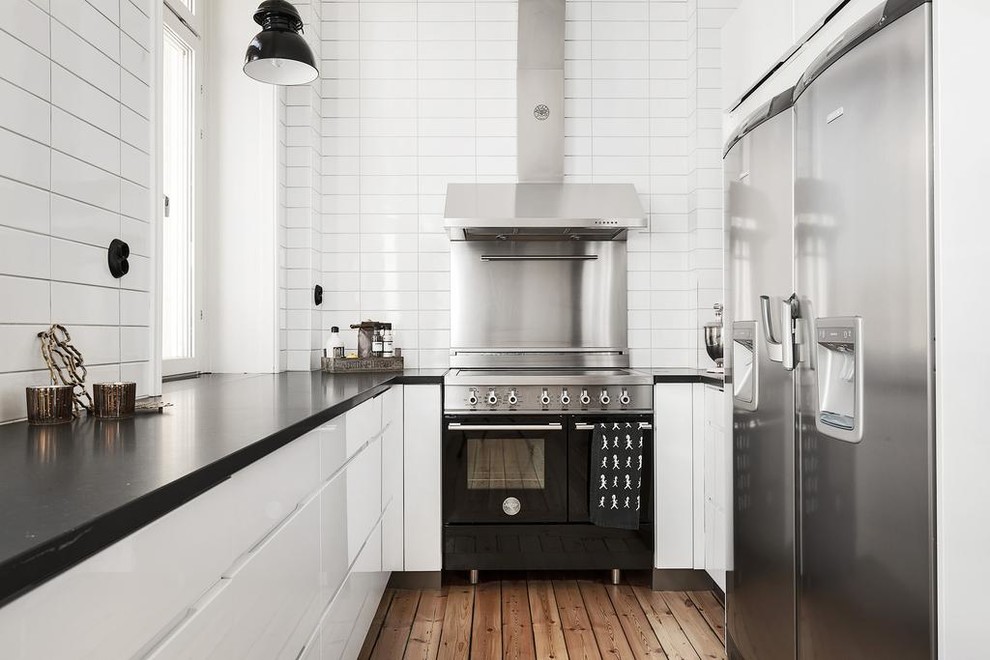 Idéer för ett mellanstort minimalistiskt u-kök, med släta luckor, vitt stänkskydd, stänkskydd i tunnelbanekakel, rostfria vitvaror och mellanmörkt trägolv
