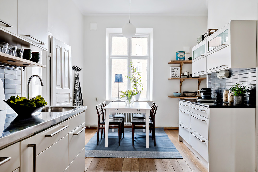 Bild på ett mellanstort skandinaviskt kök, med släta luckor, vita skåp, bänkskiva i rostfritt stål, svart stänkskydd, mellanmörkt trägolv och brunt golv