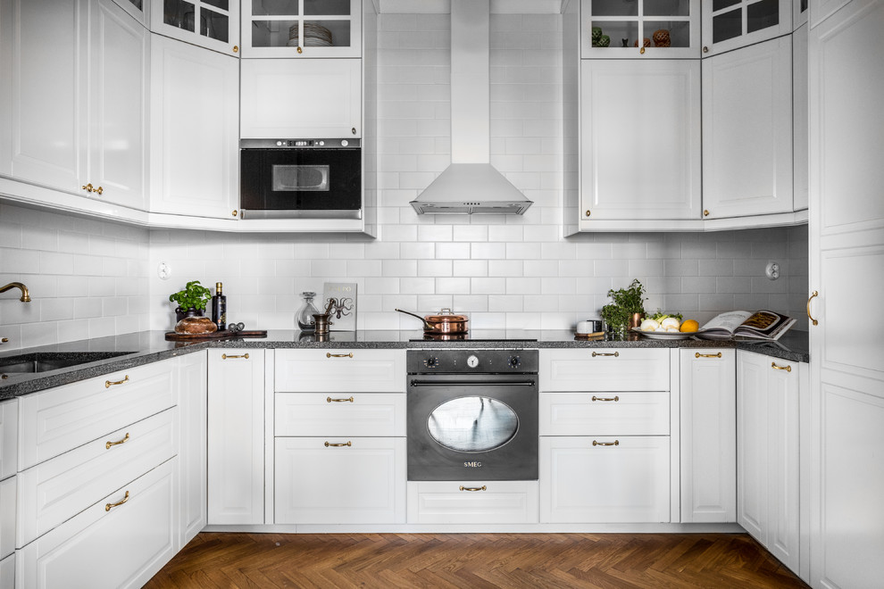 Inredning av ett minimalistiskt mellanstort grå grått u-kök, med vita skåp, en undermonterad diskho, luckor med upphöjd panel, vitt stänkskydd, stänkskydd i tunnelbanekakel, integrerade vitvaror, mörkt trägolv och brunt golv