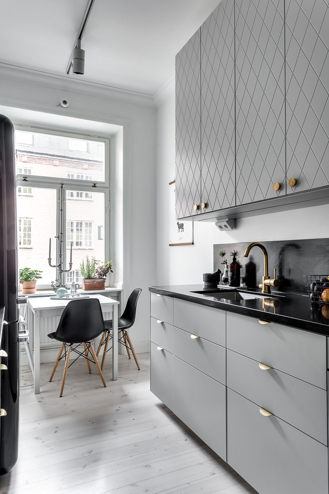 Einzeilige, Mittelgroße Nordische Küche ohne Insel mit Kassettenfronten, grauen Schränken, Granit-Arbeitsplatte, Waschbecken, Küchenrückwand in Grau und hellem Holzboden in Stockholm