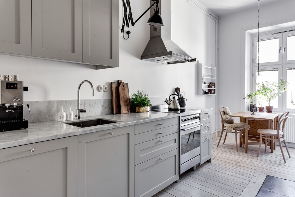 Inredning av ett minimalistiskt avskilt, mellanstort linjärt kök, med en nedsänkt diskho, luckor med upphöjd panel, grå skåp, marmorbänkskiva, rostfria vitvaror och ljust trägolv