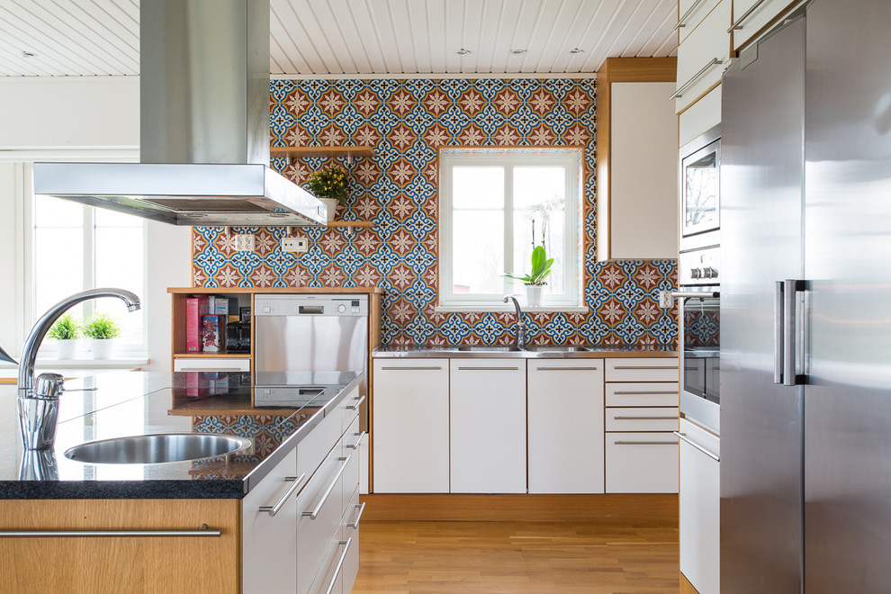 Foto på ett mellanstort medelhavsstil l-kök, med en dubbel diskho, släta luckor, vita skåp, flerfärgad stänkskydd, rostfria vitvaror, mellanmörkt trägolv, en köksö och bänkskiva i rostfritt stål